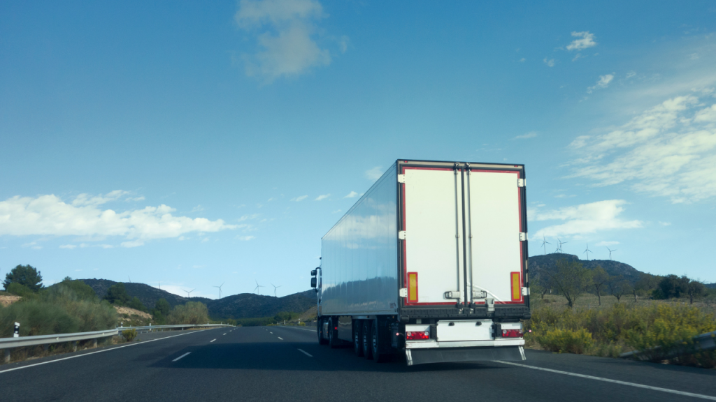 青空の下、道路をトラックが走り進んでいく画像