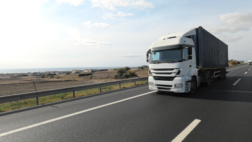 トラックが道路を走行している画像。空は晴天で周囲は田んぼが広がりのどかな背景