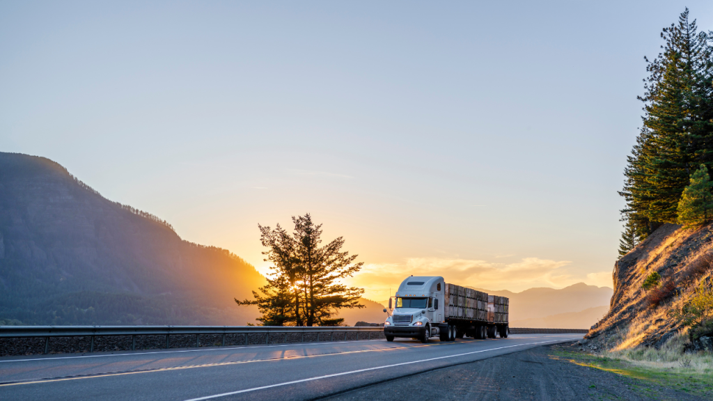 夕日が山へ沈んでいく姿を背景にトラックが道路を走行している画像